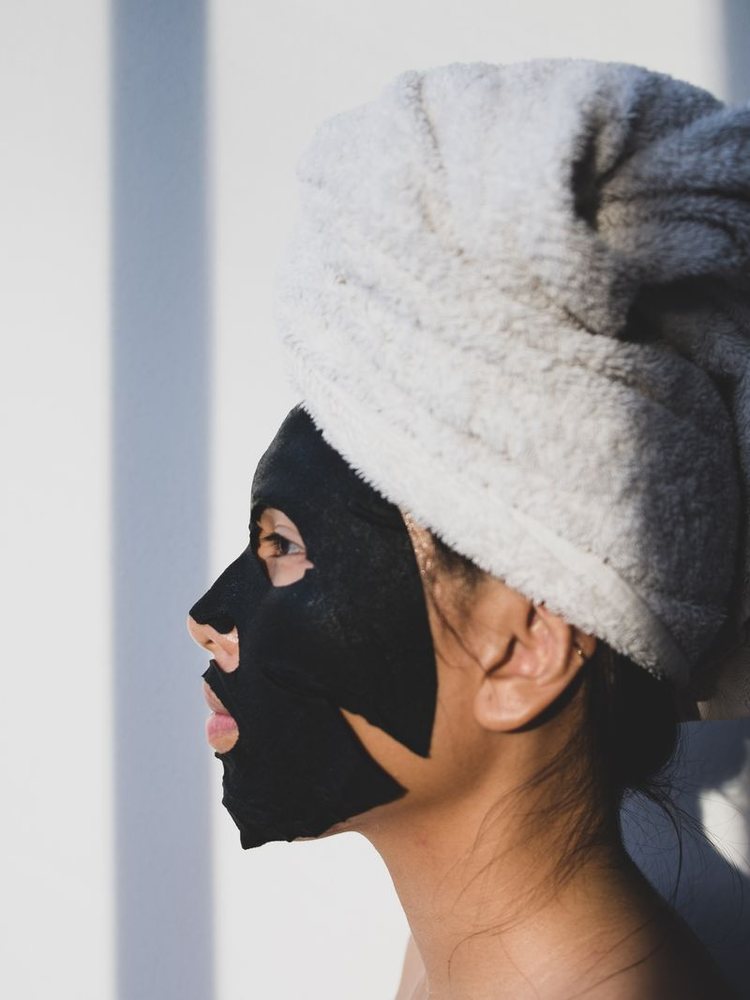 Profile of a woman in a sheet mask with a towel wrapped around her hair